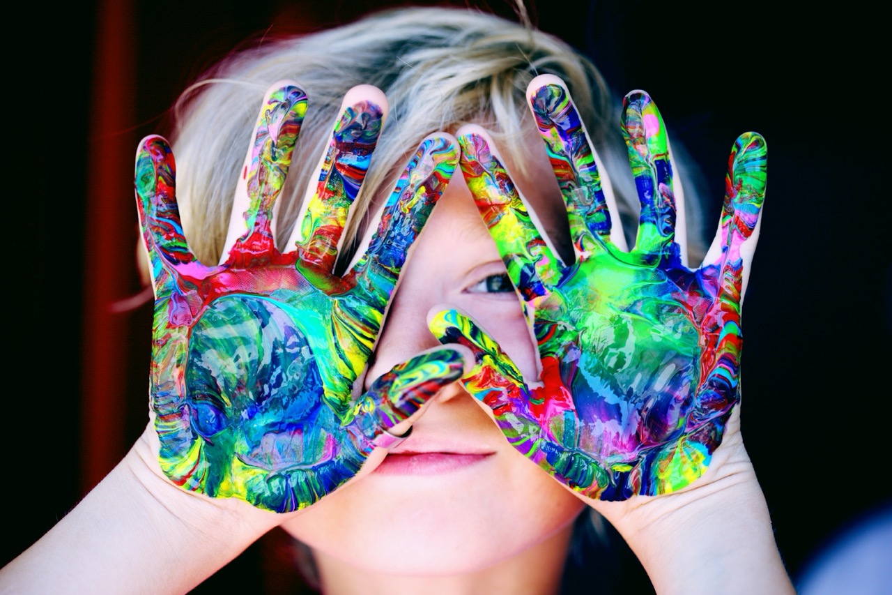 a child engaging in play based learning- his hands are covered in colourful paint!